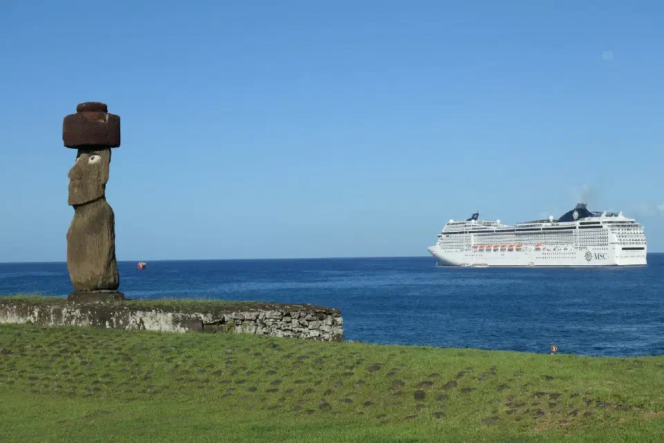 Ein Moai mit rotem Pukao blickt über das Land, den Pazifik im Rücken und im Hintergrund liegt die MSC Magnifica vor Anker.