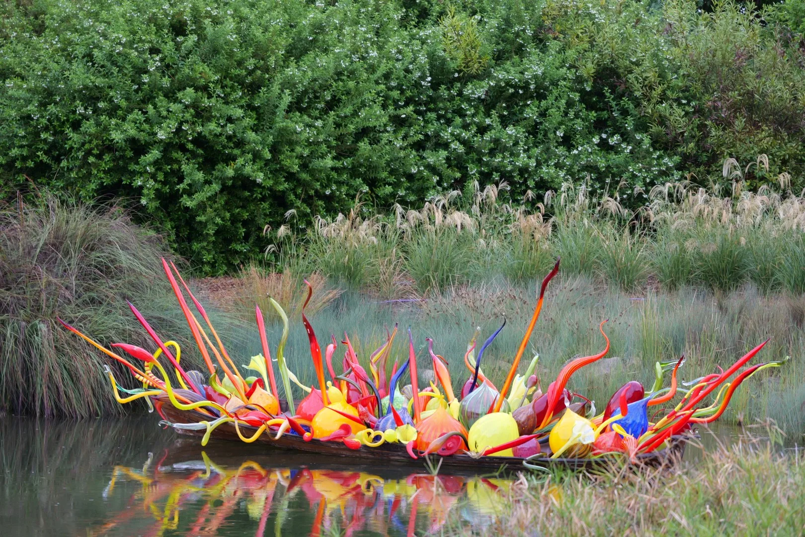 Eine farbenfrohe Glaskunstinstallation schwimmt ruhig im Wasser und setzt einen lebendigen Kontrast zur natürlichen Umgebung der Parklandschaft.