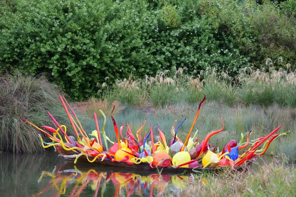 Eine farbenfrohe Glaskunstinstallation schwimmt ruhig im Wasser und setzt einen lebendigen Kontrast zur natürlichen Umgebung der Parklandschaft.