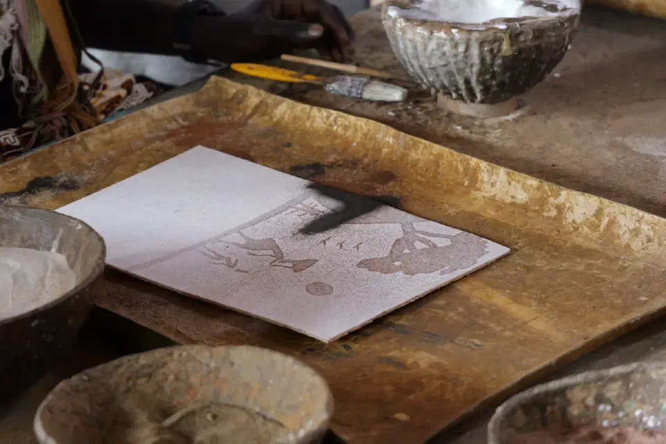 Ein Künstler arbeitet an einer traditionellen senegalesischen Sandmalerei, bei der Motive ausschließlich mit verschiedenfarbigem Sand gestaltet werden.