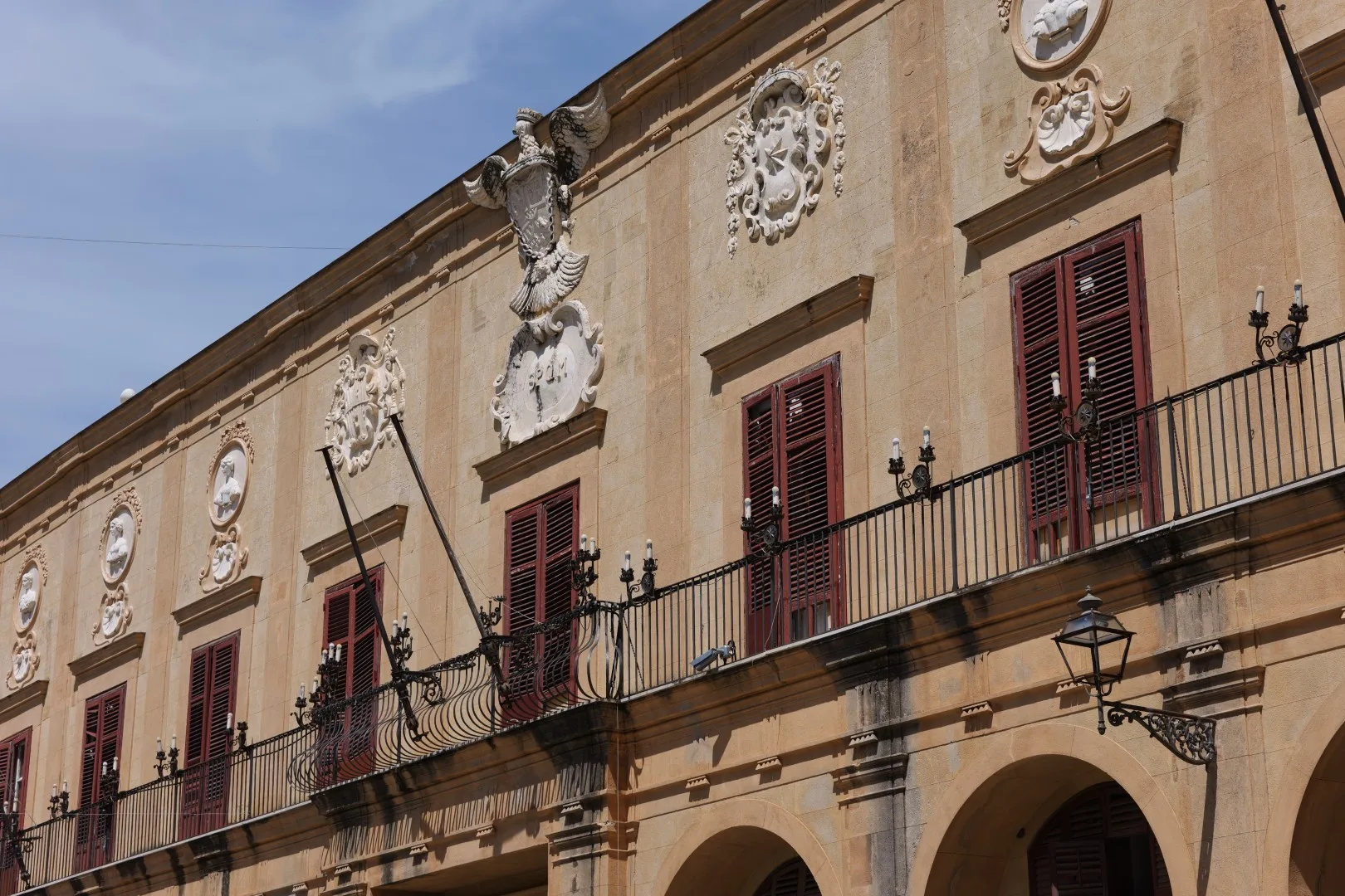 Historische Fassade eines Palastes in Palermo mit kunstvollen Wappen und typischen sizilianischen Fensterläden.