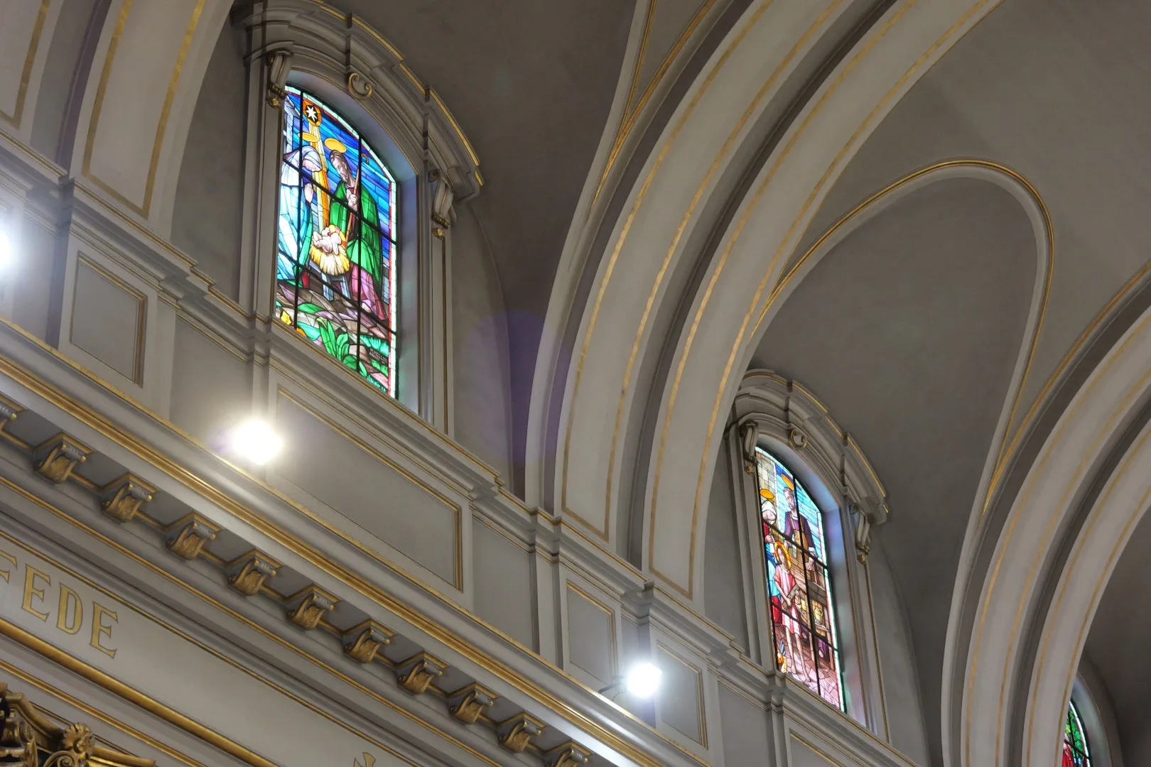Detailaufnahme aus dem Inneren einer Kirche in Civitavecchia mit farbigen Glasfenstern und harmonischer Gewölbearchitektur.